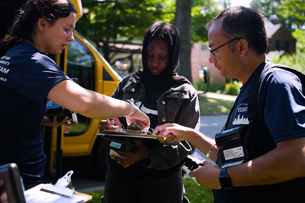 Dr. Shakya talks with two students, while collecting data outside.