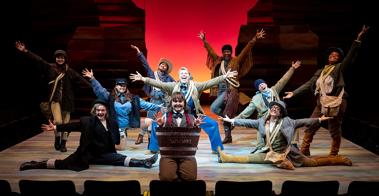 Performers smiling and posing on stage with arms spread wide